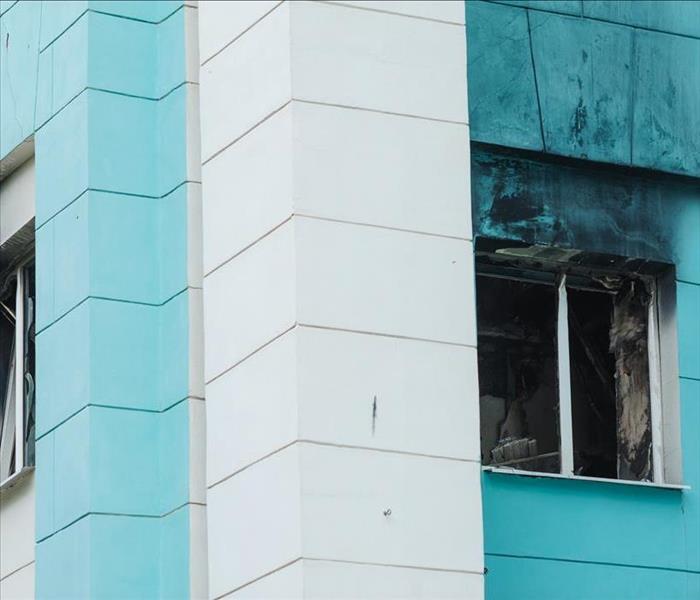 Blue building, two windows broken and window phrame with smoke damage